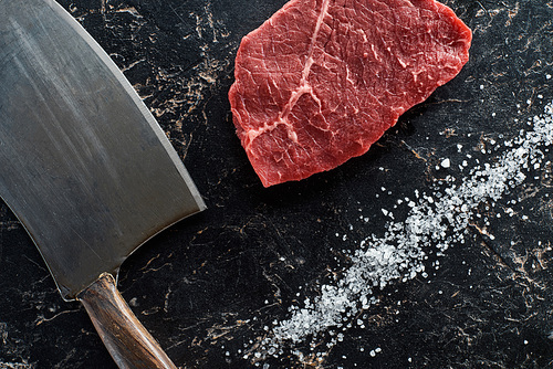 top view of uncooked beef sirloin near knife and scattered salt on black marble background