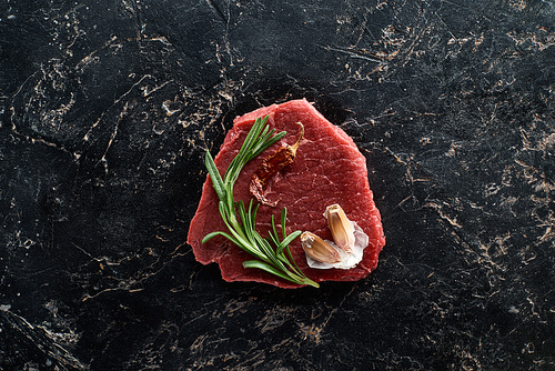 top view of raw beef steak with rosemary and garlic on black marble surface