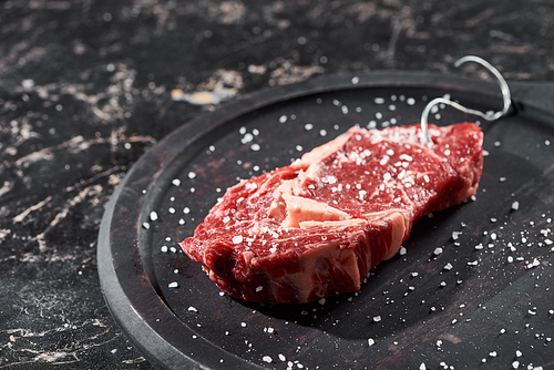 raw meat sprinkled with salt and pepper on wooden plate on black marble surface