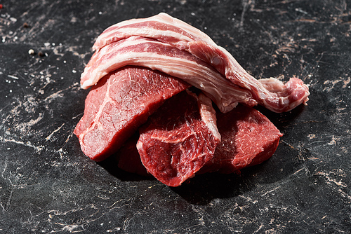 raw pork slices on beef steaks on black marble surface