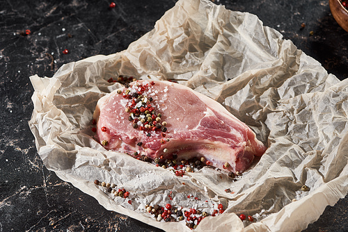 raw pork steak sprinkled with salt and pepper on parchment paper on  marble surface