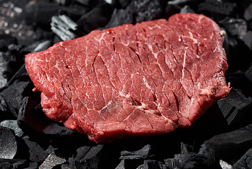 close up view of raw sirloin on black charcoal pieces