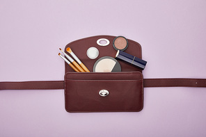 top view of decorative cosmetics near bag isolated on violet