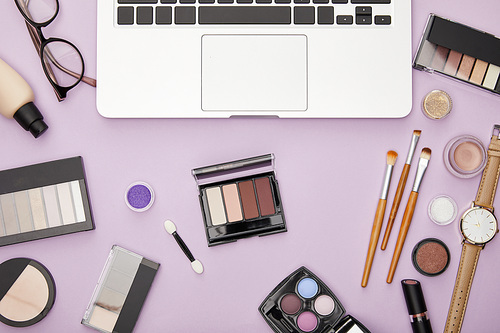 top view of laptop near decorative cosmetics isolated on violet