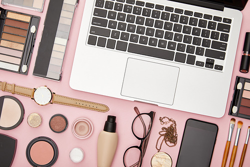top view of laptop near decorative cosmetics and glasses isolated on pink