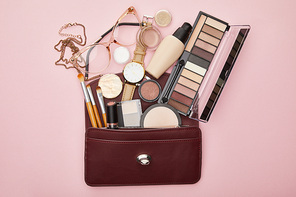 top view of brown bag near decorative cosmetics and watch isolated on pink