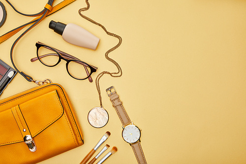top view of bag near glasses, necklace and watch isolated on yellow