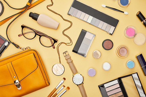 top view of bag near glasses and decorative cosmetics isolated on yellow
