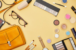 top view of bag near decorative cosmetics and glasses isolated on yellow