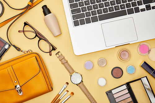 top view of laptop near glasses and decorative cosmetics isolated on yellow