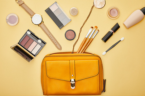 top view of bag near eye shadow and watch isolated on yellow
