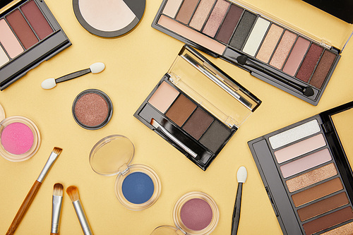 top view of set with brown eye shadow near cosmetic brushes isolated on yellow