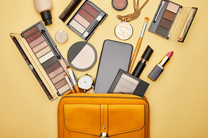 top view of bag with decorative cosmetics and smartphone with blank screen isolated on yellow