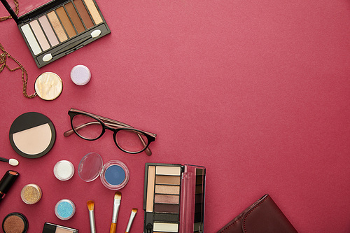 top view of decorative cosmetics near glasses and necklace on crimson