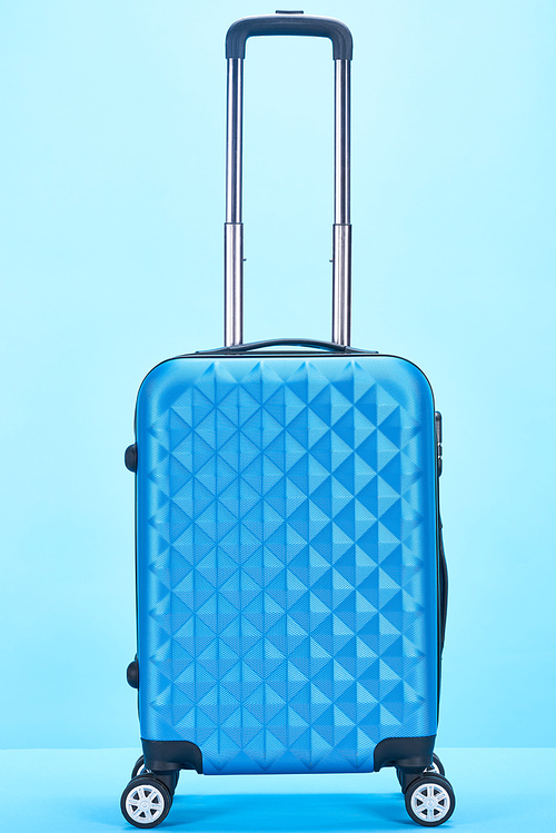 blue colorful travel bag with handle on wheels on blue background