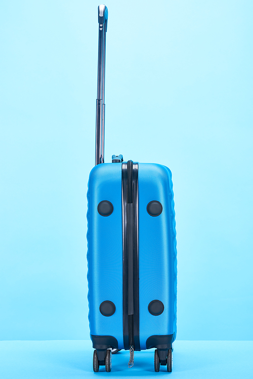 blue colorful travel bag with handle on wheels on blue background with copy space