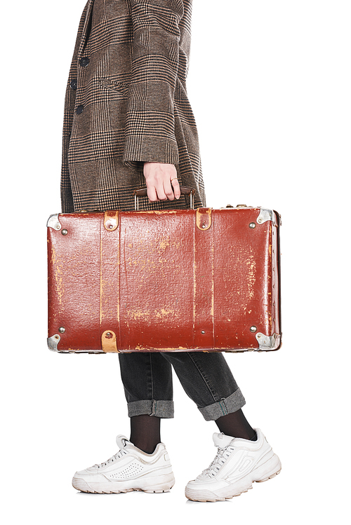 cropped view of woman in plaid coat walking with vintage weathered suitcase isolated on white