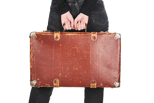 partial view of woman in jeans holding vintage leather suitcase isolated on white