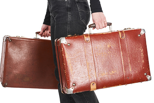 cropped view of woman in jeans holding vintage weathered suitcases isolated on white