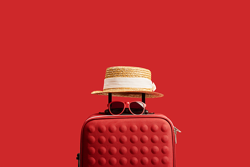 red travel bag with straw hat and sunglasses isolated on red