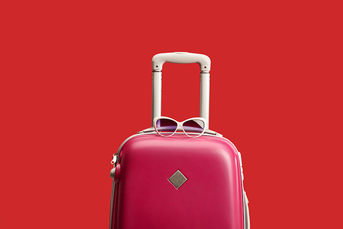 red colorful travel bag with sunglasses isolated on red