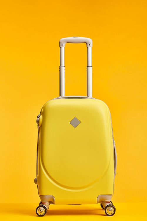 yellow travel bag with handle and wheels isolated on orange