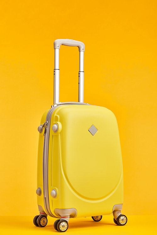 yellow travel bag with handle on wheels isolated on orange