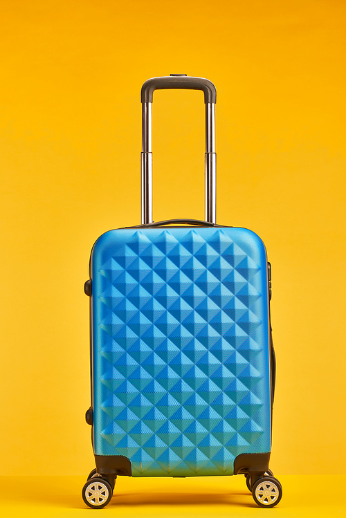 blue travel bag with handle on wheels isolated on orange