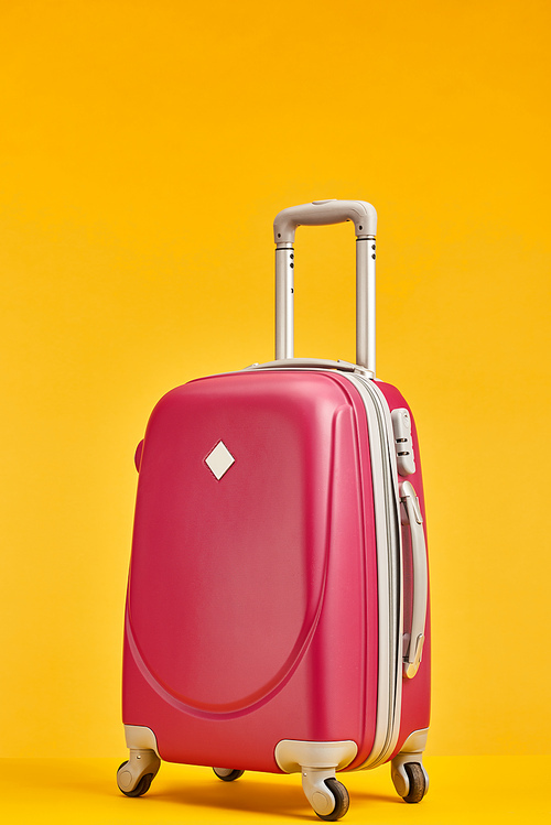 red suitcase with handle on wheels isolated on orange