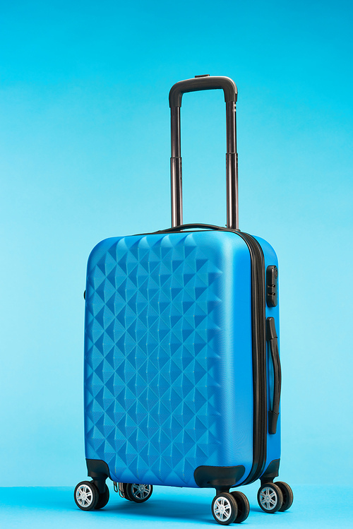 blue suitcase with handle on wheels on blue background