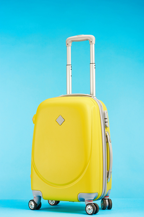 yellow colorful travel bag with handle on wheels on blue background
