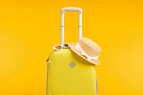 yellow colorful travel bag with sunglasses and straw hat isolated on yellow