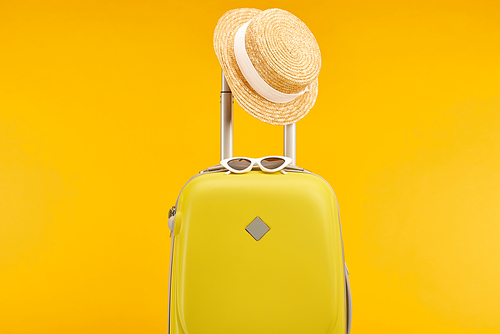 yellow colorful travel bag with sunglasses and straw hat on handle isolated on yellow