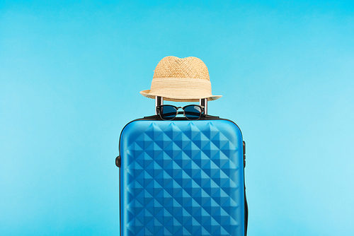 blue colorful travel bag with handle, sunglasses and straw hat isolated on blue