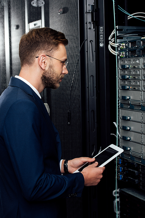 handsome businessman in glasses holding digital tablet and looking at database in server rack