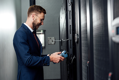 side view of happy businessman standing with reflectometer in server room