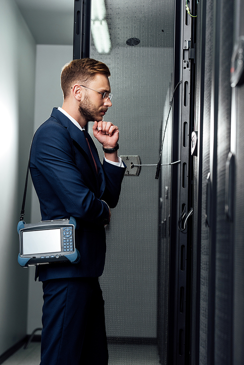 side view of pensive businessman standing with reflectometer in server room