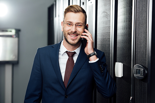 cheerful businessman in glasses talking on smartphone in server room
