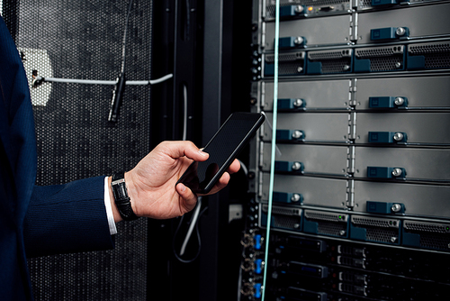 cropped view of man holding smartphone with blank screen in server room