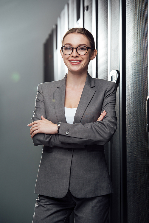cheerful businesswoman in glasses standing with crossed arms in data center