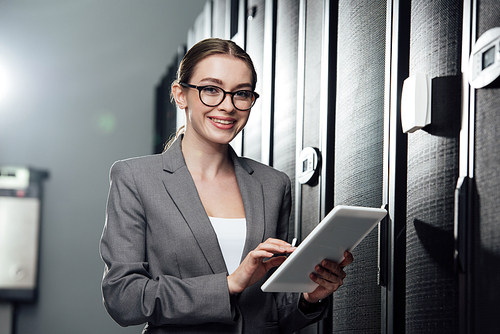selective focus of cheerful businesswoman holding digital tablet in server room
