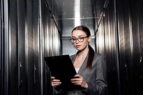 attractive businesswoman in glasses looking at clipboard in data center