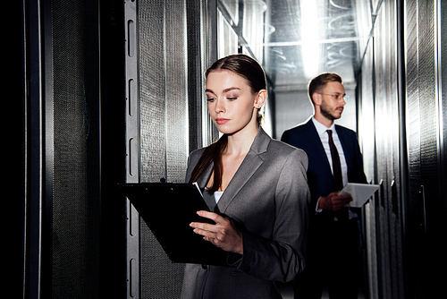 selective focus of attractive businesswoman holding clipboard near businessman in data canter