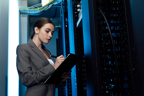 attractive businesswoman writing while holding clipboard in server room