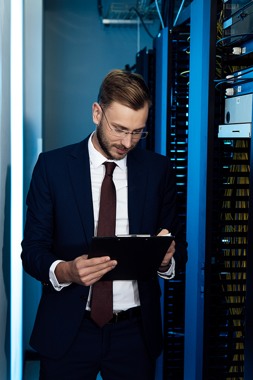 handsome businessman in glasses holding clipboard in data center