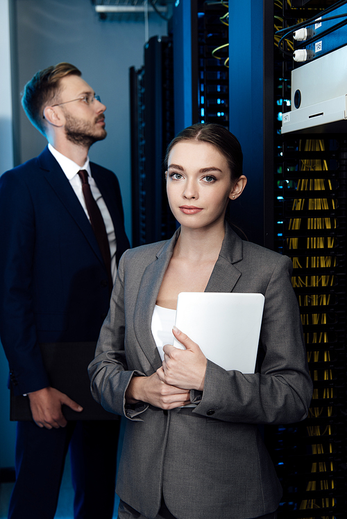 selective focus of attractive businesswoman holding digital tablet near bearded businessman in data center