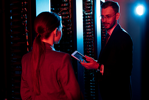 selective focus of handsome bearded businessman holding digital tablet near woman in server room