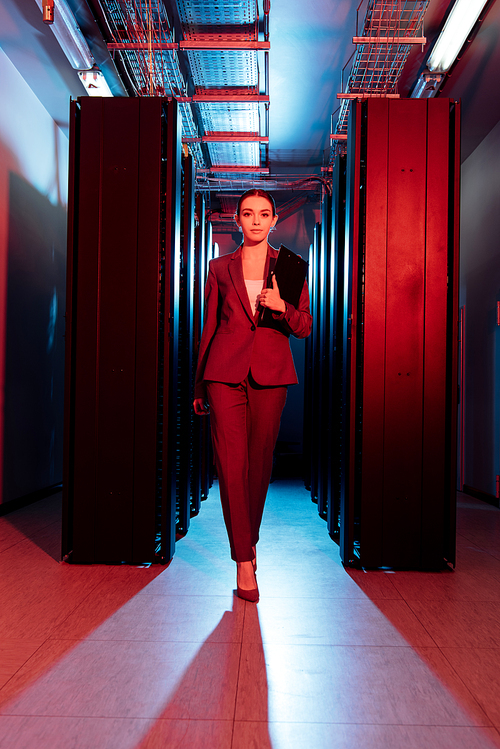 attractive businesswoman holding clipboard while walking in server room