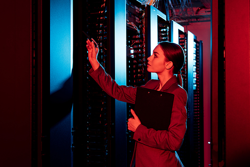 side view of businesswoman holding clipboard and looking at server room