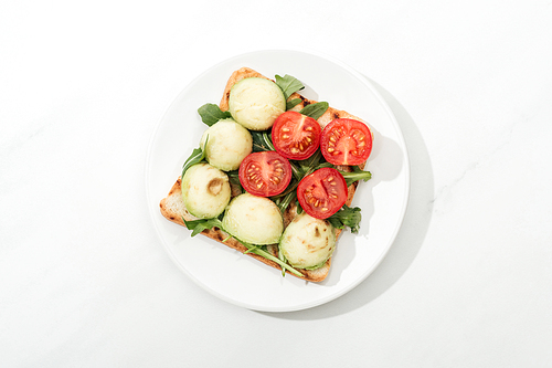 Top view of toast with cherry tomatoes and arugula on plate on white surface